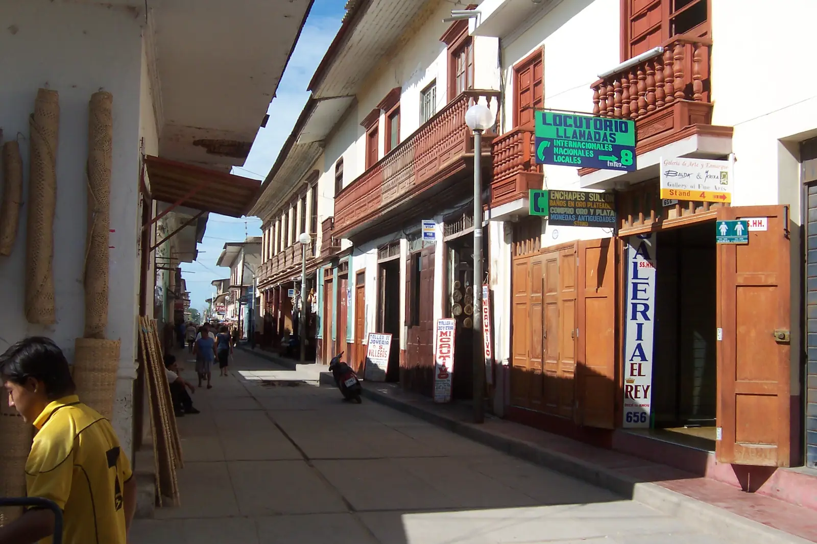 Una calle soleada de Catacaos con casas de balcones de madera y tiendas